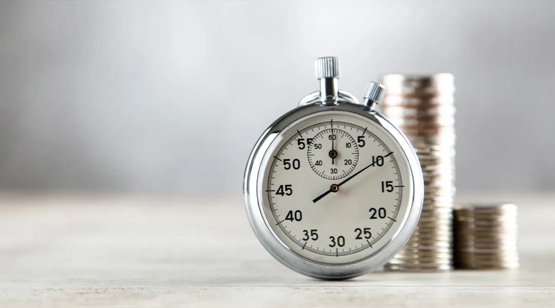A stopwatch and stacks of coins on a wooden table, symbolizing time and financial transactions.