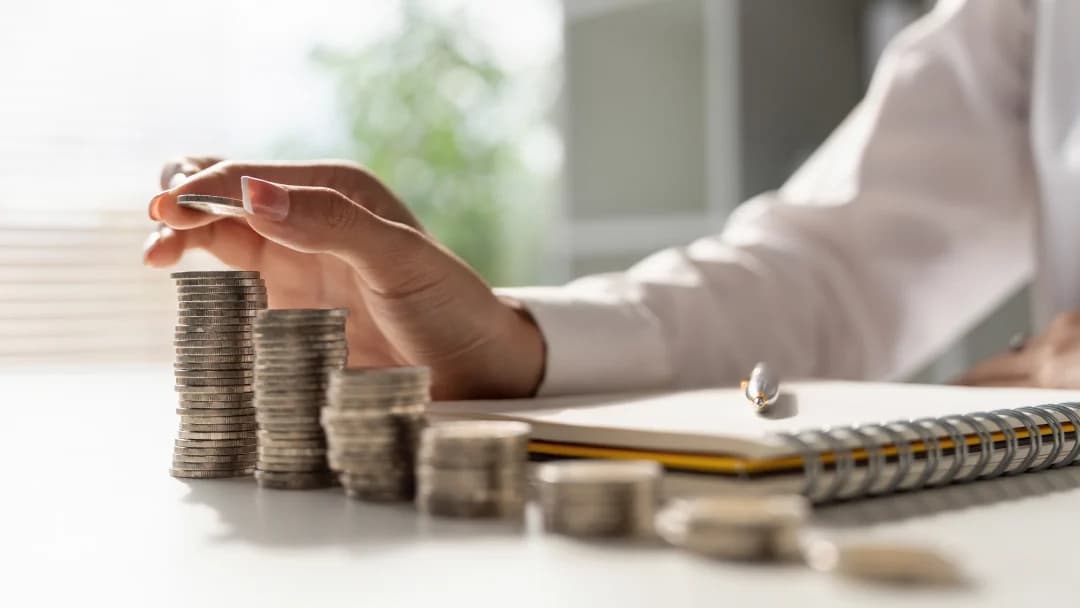 Businessman writing in a notebook, surrounded by stacks of coins, symbolizing financial investment and strategic planning.