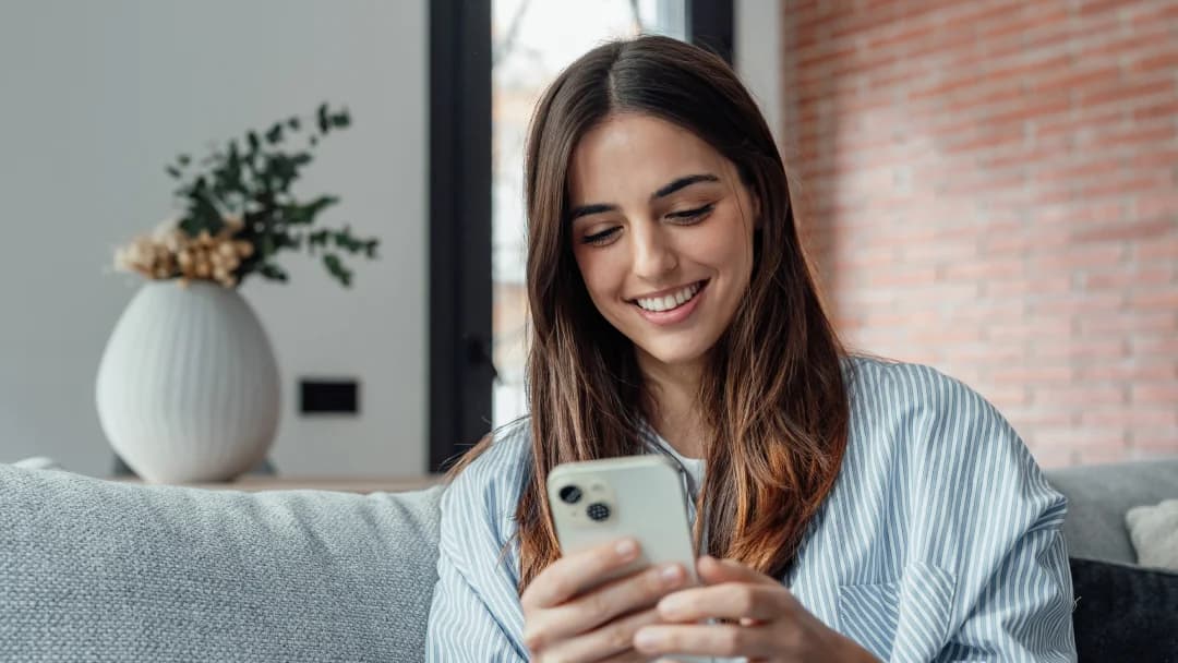 A woman smiles while using her phone, representing the ease of accessing no credit check loans.
