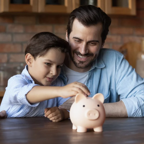 A man and a boy are depositing money into a piggy bank, symbolizing the importance of financial investment.
