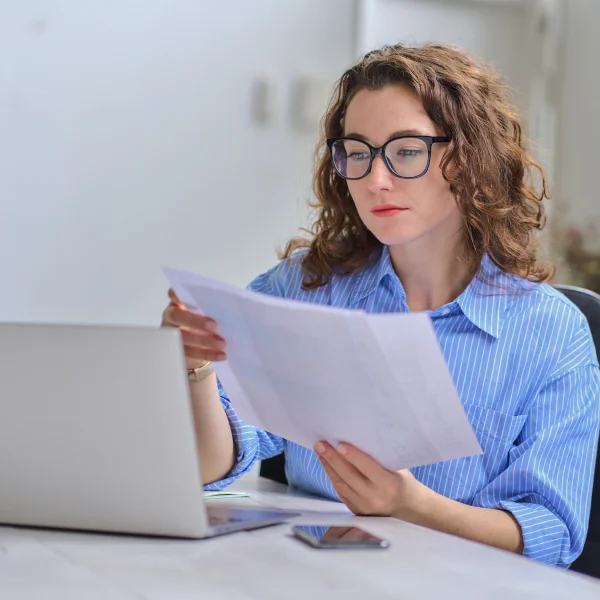 A woman in glasses reviews a financial investment document with a focused expression.