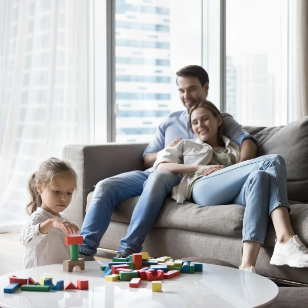 A family on a couch, with a child engaged in play using colorful toy blocks, symbolizing togetherness and support.