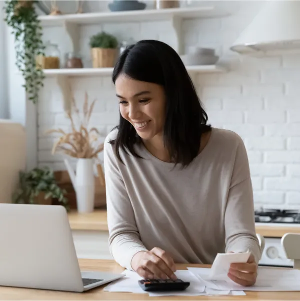 A woman sits at her kitchen table, using a laptop and calculator to manage her finances after securing a loan with bad credit.
