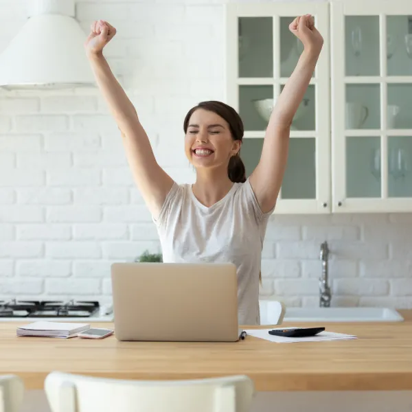 A woman sitting at a table with her arms raised and a laptop computer.