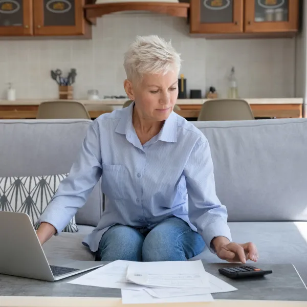 A woman sitting on a sofa with a laptop and some papers.