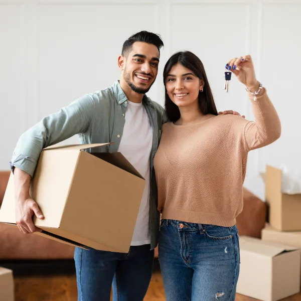 A young couple holding a key and moving boxes, symbolizing their new home with a private mortgage.